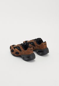 Baskets Nike avec un dessus en daim marron, des accents en maille noire, une forme arrondie et une semelle en caoutchouc noir avec un coussin d'air visible.