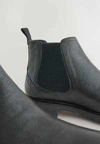 Botas Chelsea de cuero negro con panel lateral elástico texturizado y detalles de brogue en la puntera. Acabado liso con un tacón bajo.