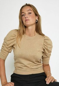 Bežový pletený svet sweater s krátkymi naberanými rukávmi a priliehavým strihom. Hladká textúra s rebrovaným výstrihom a lemom.