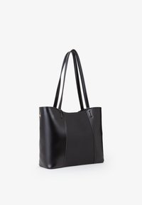 Borsa tote nera che presenta un mix di pelle liscia e tessuto testurizzato. Ha due manici lunghi e un design minimalista senza hardware visibile.