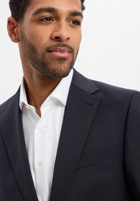 Marineblazer mit Reverskragen, Ein-Knopf-Verschluss und einer Brusttasche, kombiniert mit einem makellos weißen Hemd mit Knopfdetails.