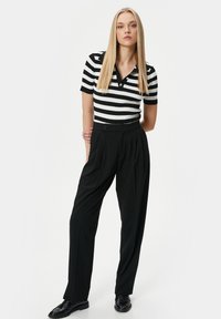 Svartvitrandig kortärmad polotröja, tillsammans med högmidjade svarta plisserade byxor och svarta finskor.