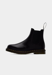 Bota Chelsea em pele preta com painéis laterais elásticos, costura amarela, aba para puxar e sola grossa de borracha. Acabamento liso, forma elegante.