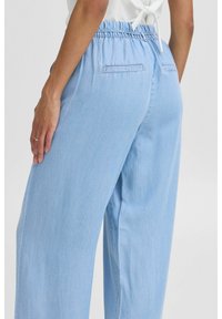 Svijetloplave, hlače visokog struka s elastičnom waistband, opuštenog kroja i dva stražnja džepa od meke, denimu slične tkanine.