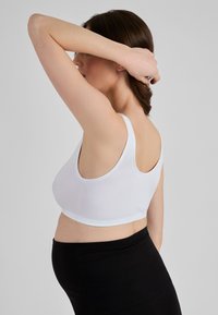 Balta medvilnė braziliška liemenėlė su plačiomis petnešėlėmis ir kreiva iškirpte, derinama su juodomis aukšto juosmens legginsomis. Lygus paviršius ir paprastas dizainas.