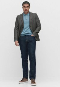 Grå rutigt blazer, ljusblå polo skjorta, mörka jeans och bruna mockaskor. Modell står mot en vit bakgrund.