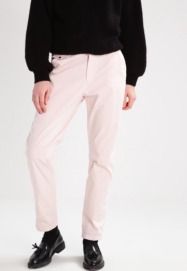 Ljusrosa byxor i ett slätt tyg med rak passform. Kombinerat med en svart, strukturerad tröja och glänsande svarta skor.