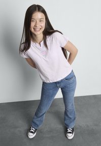 Světlofialové tričko Henley s krátkými rukávy a malým logem, doplněné modrými zvonovými džíny a černými teniskami s bílými podrážkami.