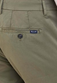 Pantaloni in cotone verde oliva con una texture liscia, dotati di una tasca posteriore con un bottone nero e un'etichetta blu con il marchio.