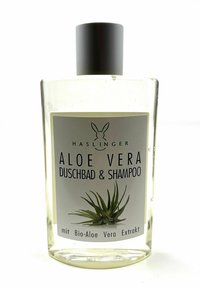 Durchsichtige rechteckige Flasche mit schwarzem Deckel, beschriftet "Aloe Vera Duschbad & Shampoo." Enthält Flüssigkeit mit einer Aloe-Pflanze Grafik und Text.