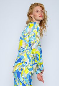 Kolorowa, wzorzysta bluzka z niebieskimi, żółtymi i beżowymi zawijasami. Lekki materiał z długimi rękawami i luźnym krojem, uzupełniona guzikami.