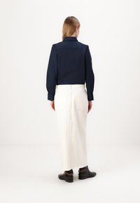 Marineblå langermet skjorte med knappe mansjetter, kombinert med et høydefinert hvitt denimskjørt. Svarte ankelboots med gullkjede-detalj.