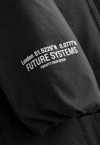 Mustas jopevarrukas valge teksti detailideks: "London 51.5229'N 0.0777'W", "FUTURE SYSTEMS" ja "TWENTY FOUR SEVEN". Pehme tekstuur.