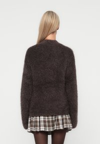 Donkerbruin donzig sweater met lange mouwen, ronde hals en zachte textuur, gecombineerd met een geruit rokken.