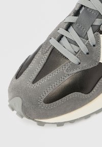 Pantof sport din piele întoarsă gri și piele neagră, cu panouri din plasă, șireturi gri și talpă exterioară din cauciuc texturat. Are cusături vizibile și vârf rotunjit.