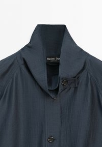 Mörkgrå ribbstickad tygjacka med hög krage, knappstängning och Massimo Dutti-märke synligt inuti kragen.