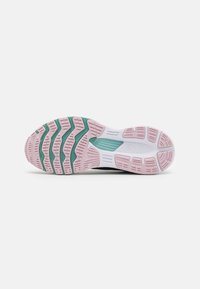 Semelle de chaussure de sport en noir et blanc avec des accents rose et vert. Présente des motifs de semelle texturés pour l'adhérence et la flexibilité.