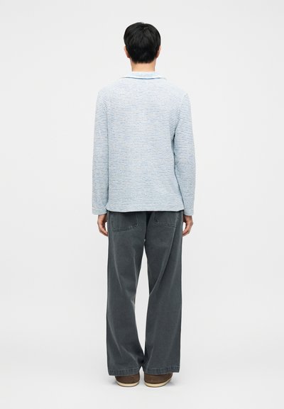 Pull à rayures bleu clair avec manches longues et col, associé à un pantalon large gris foncé. Le matériau semble doux et texturé.