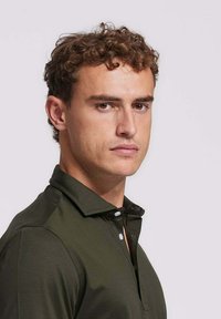 Donkergroene polo gemaakt van een soepele stof, met een kraag, een drukknoopsluiting en korte mouwen.