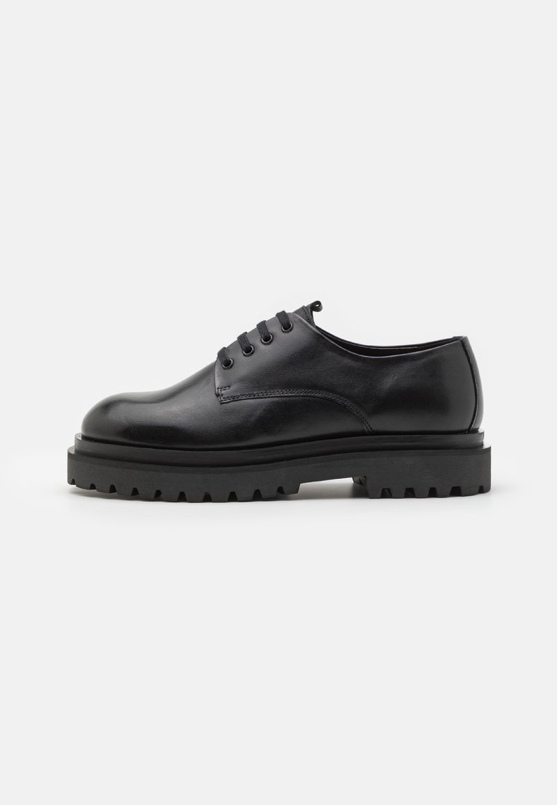 Chaussure noire en cuir à lacets avec semelle épaisse à rainures, talon bas et bout rond, vue de profil sur fond blanc uni.