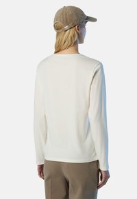 Camicia bianca a maniche lunghe con scollatura tonda, abbinata a un cappello beige con texture. La camicia presenta un fit rilassato e dettagli delle cuciture sottili.