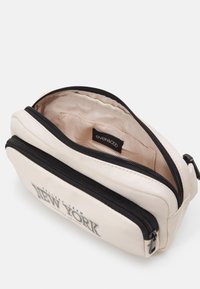 Trousse beige avec deux fermetures éclair noires, texte "New York" sur la poche avant, doublure intérieure en tissu beige avec une étiquette "Even&Odd" visible.