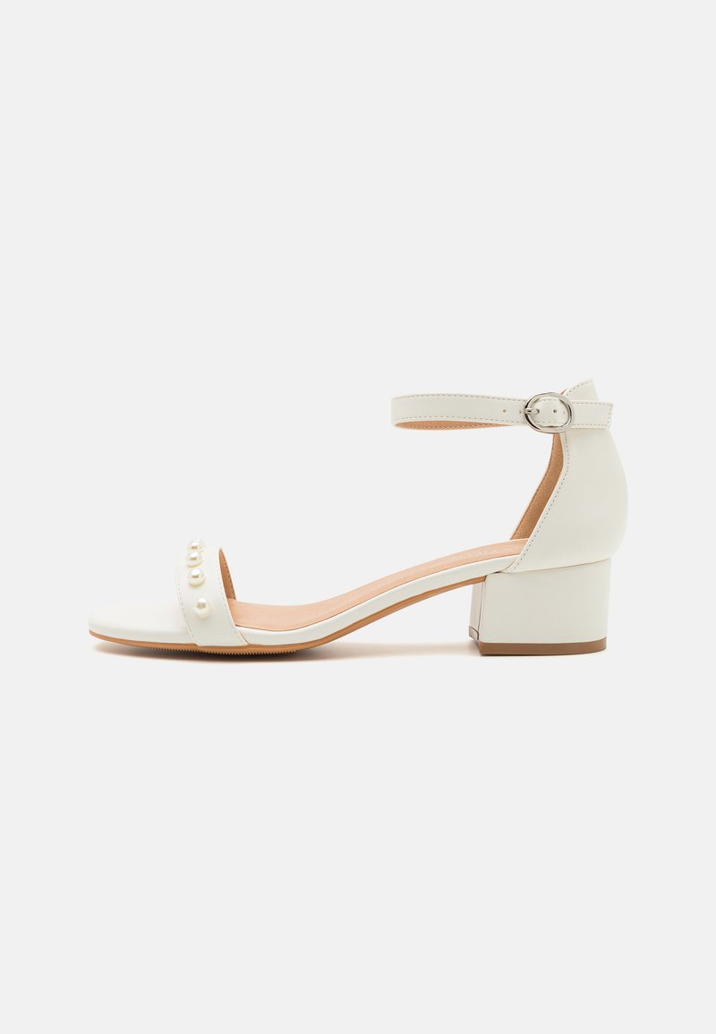 Hvit åpen-tå heeled sandal med en chunky blokk hæl, med en stropp rundt ankelen og dekorative perlelignende detaljer på tåen.