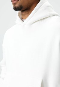 Witte hoodie met een capuchon met trekkoord, grote voorkantzak, zachte textuur en geribbelde boorden. Eenvoudig, minimalistisch ontwerp.