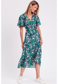 Abito midi stampato floreale in verde con maniche a sbuffo corte, vita definita e orlo leggermente arricciato, abbinato a sneakers bianche.