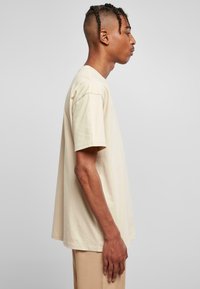 Beige bomulls t-skjorte med korte ermer og en avslappet passform, vist fra siden. Har en rund halslinning og minimal sydetaljer.