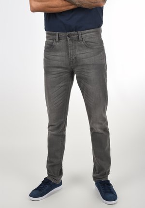 Grijze spijkerbroek met een rechte snit, vijf zakken, subtiele slijtage en een klassieke knoopsluiting, gecombineerd met donkerblauwe sneakers.