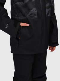 Person in schwarzer wasserdichter Jacke und Hose, mit einer Hand teilweise in der Jackentasche, die ein Handgelenkband mit der Aufschrift "10K" zeigt.