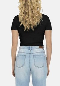 Top negro de mangas cortas combinado con jeans de tiro alto en azul claro. Los jeans tienen dos bolsillos traseros y una etiqueta de piel color marrón en la cintura.