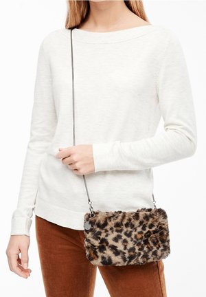 Osoba ubrana w biały długi rękaw i brązowe spodnie, trzymająca małą torebkę na ramię z imitacji futra w cętki lamparta z cienkim paskiem.