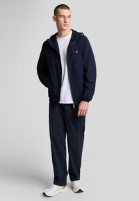 Marineblå hættetrøje med to frontlommer, båret over en hvid t-shirt, parret med marineblå joggers og hvide sneakers. Rene linjer og letvægtsstof.