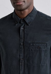 Camicia nera da uomo con bottoni, realizzata in tessuto morbido e testurizzato, con colletto, tasca frontale e bottoni scuri. Presenta un design informale.