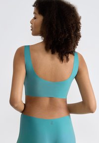 Türkisfarbener nahtloser BH mit breitem Bündchen und Scoop-Rücken-Design, hergestellt aus glattem, dehnbarem Material mit matter Oberfläche.