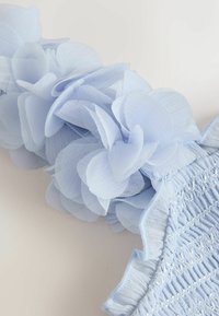 Hele sinised kangast lilled kinnitatud tekstuurse, voldilise äärega rõivaesemele või aksessuaarile.