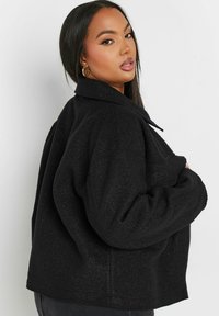 Svart fleecejacka med krage, oversize passform och sidodragkedjedetalj. Mjuk textur och kraftiga, avslappnade ärmar.