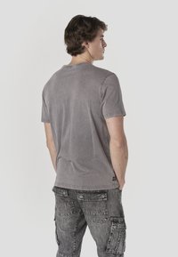 Gray cotton t-shirt with short sleeves and a relaxed fit, paired with black denim cargo pants featuring multiple pockets and a distressed texture.