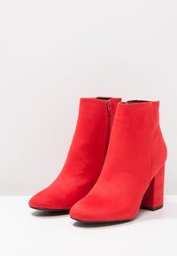 Czerwone zamszowe botki za kostkę z czubkiem w kształcie spiczastym i słupkowym obcasem. Posiadają boczny zamek błyskawiczny do zapinania. Gładka faktura i minimalistyczny design.