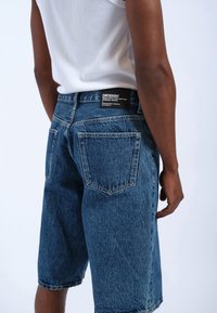 Shorts de mezclilla azul con un corte relajado. Presentan una cinturilla alta, bolsillos traseros y una etiqueta de marca en la parte trasera. Tejido texturizado.
