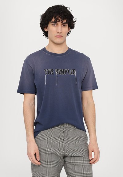 Námořnická modrá bavlněná tričko s potiskem "THE KOOPLES" v bílém obrysu, v kombinaci s kostkovanými kalhotami v černé a bílé barvě. Krátké rukávy, kulatý výstřih.