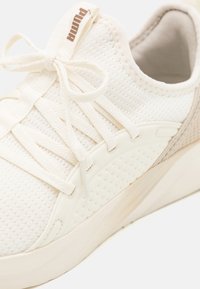 White mesh sneaker with cream accents, featuring flat laces, a textured sole, and a padded collar for comfort and support.