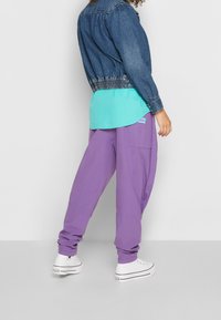 Jeansjacka, ljusblå skjorta och lila cargobyxor. Vita sneakers med svarta detaljer och böjda fickor på byxorna skapar kontrast.