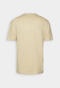 T-shirt beige à manches courtes et col rond, montré de dos sur un fond uni gris clair.
