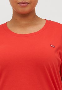 Punainen puuvillapaita, jossa on pyöreä kaula-aukko ja lyhyet hihat, sekä pieni Levi's-logo-painatus vasemmalla puolella etumuksessa. Pehmeä tekstuuri.