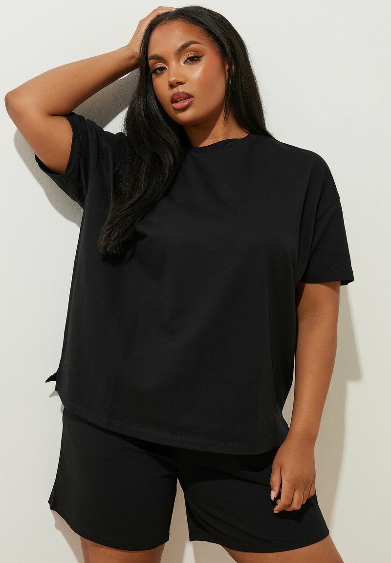 Svart bomullströja med avslappnad passform och korta ärmar, tillsammans med matchande svarta shorts. Slät textur och enkel design, utan mönster.