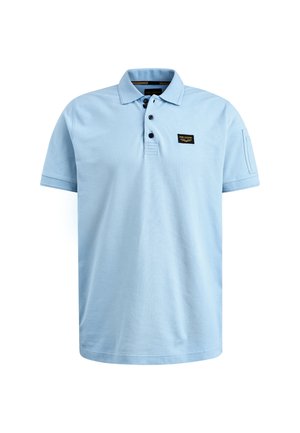 Vaaleansininen puuvillapolo, jossa on klassinen kaulus, kolme nappia ja pieni musta etiketti rintataskussa. Lyhyet hihat.