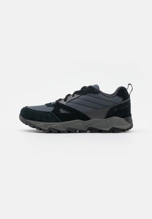 Zwart-grijze veterschoenen voor wandelen met een gestructureerde zool, bovenwerk van stof en suède, en een trekgaatje aan de hiel, zijaanzicht.